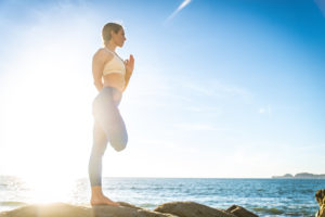 Woman training yoga on the beach at sunset