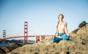 Woman training yoga on the beach at sunset